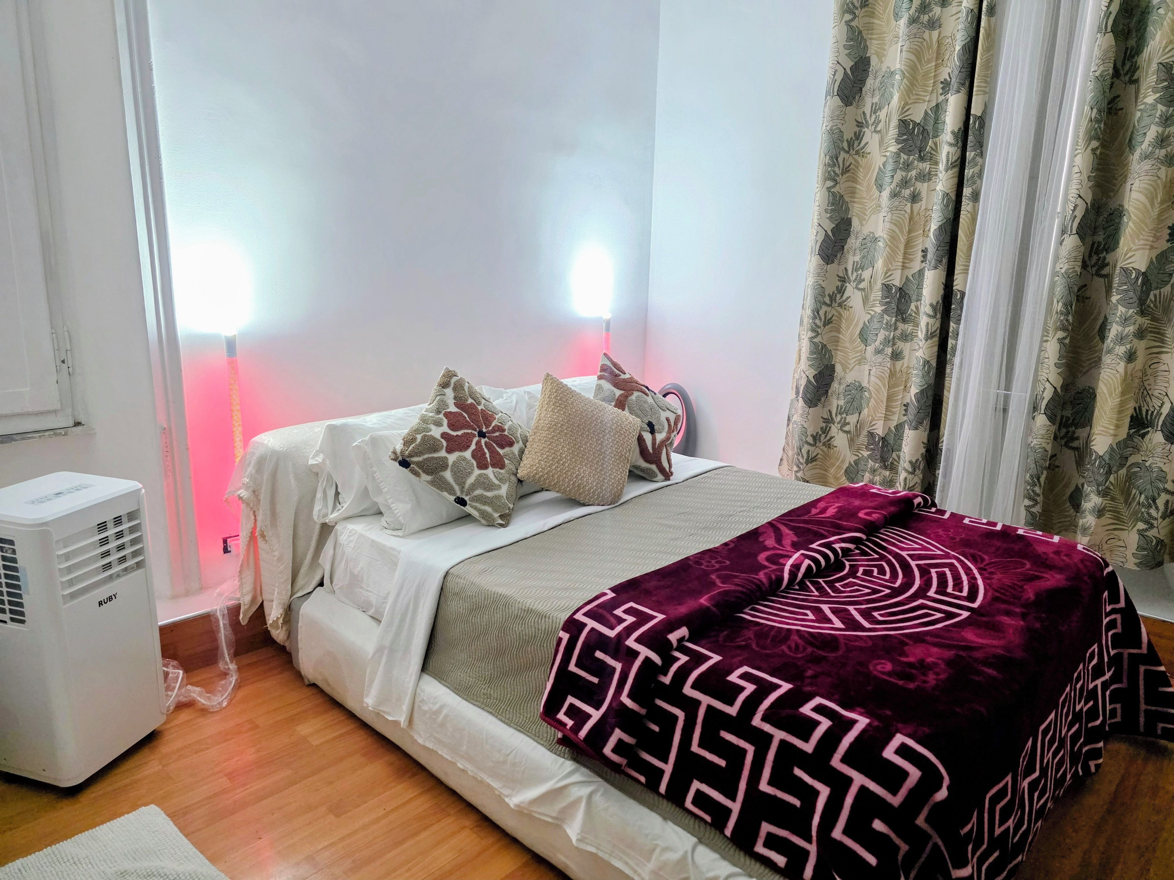 Un dormitorio con cama, almohadas, una colcha, un calentador y cortinas.