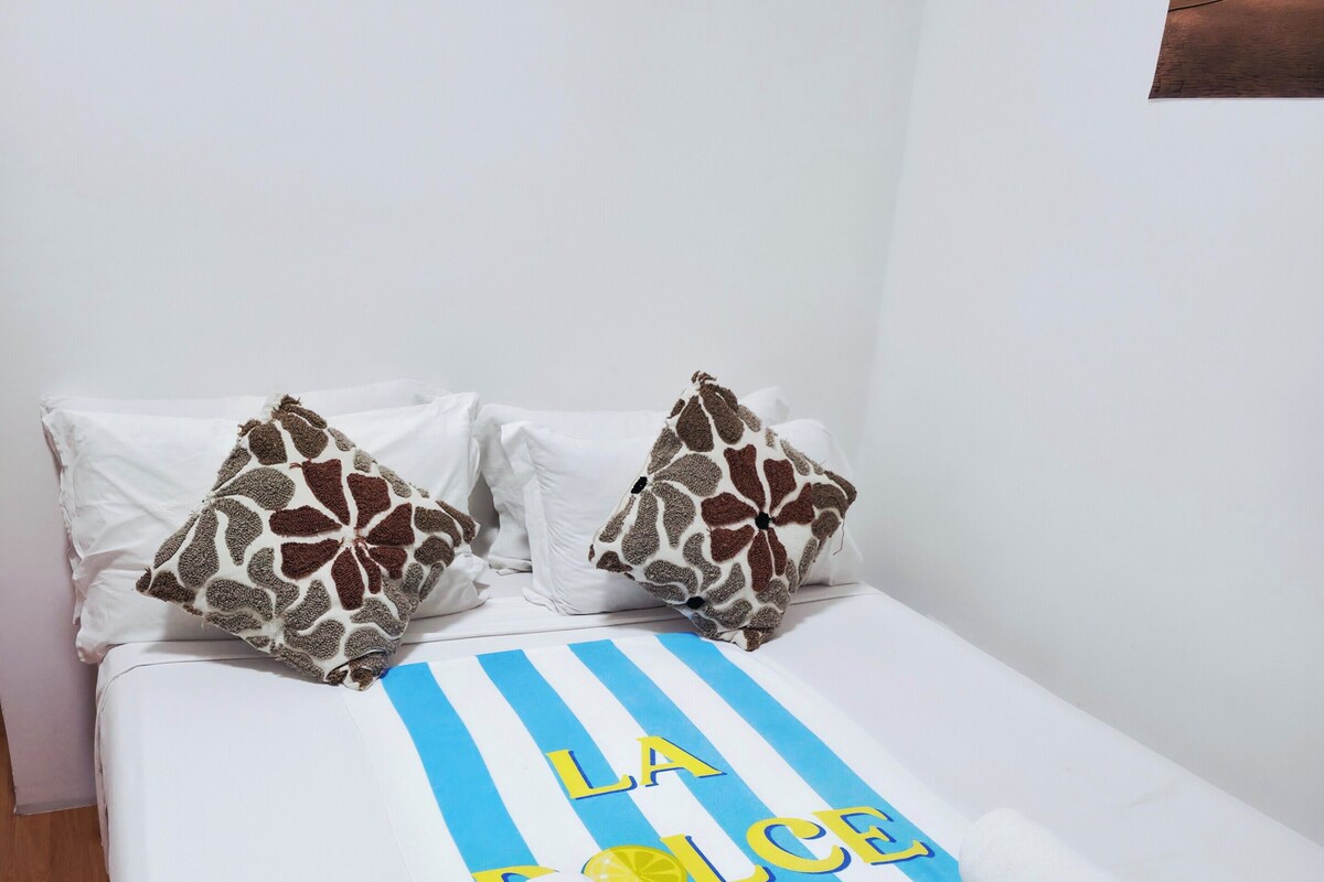 Una cama con una colcha a rayas, dos almohadas con estampado de jirafa y una toalla enrollada.