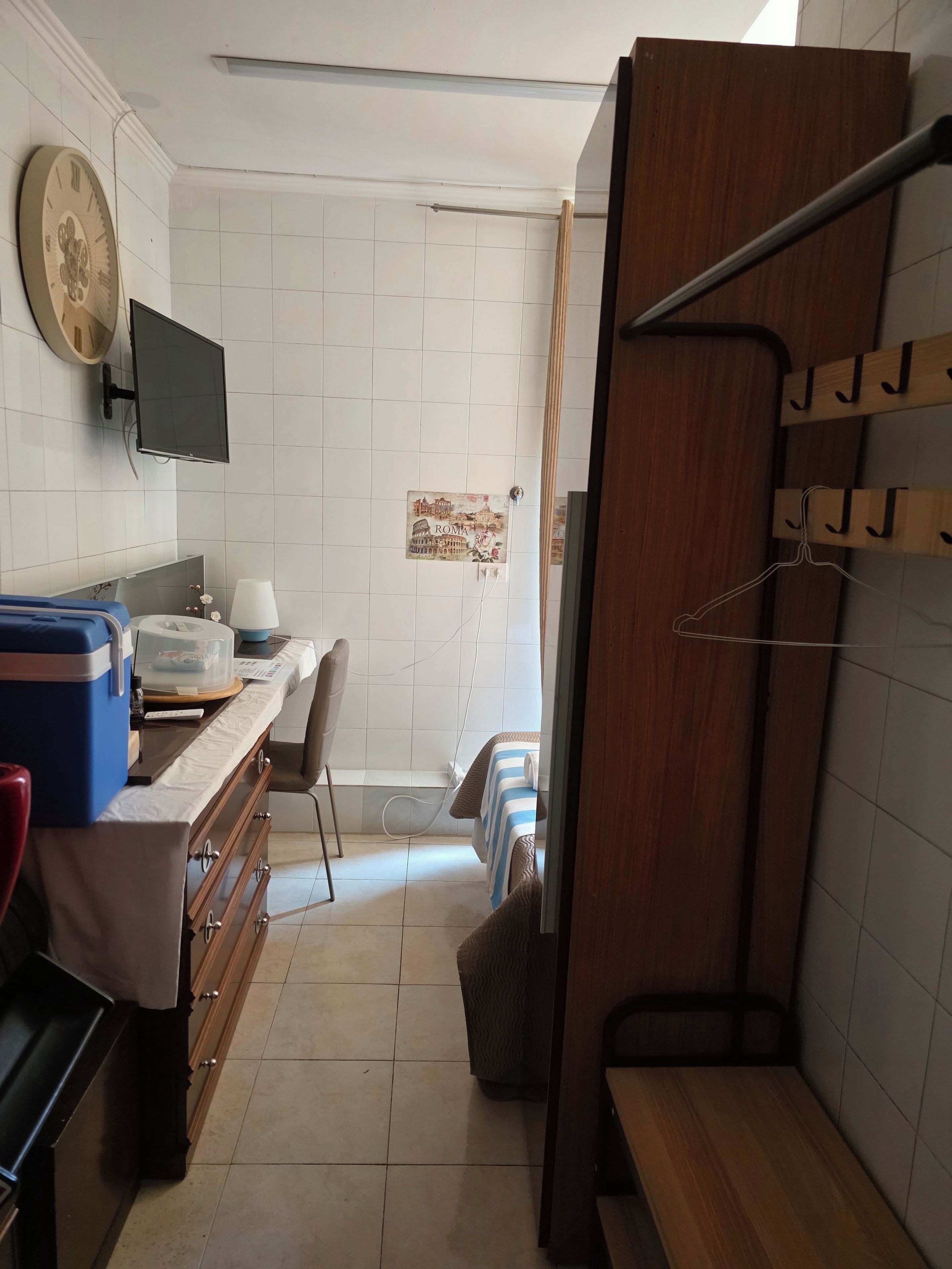 Een hotelkamer met een bed, een bureau met een computer, een televisie en een badkamer met een douche en een handdoekhouder.