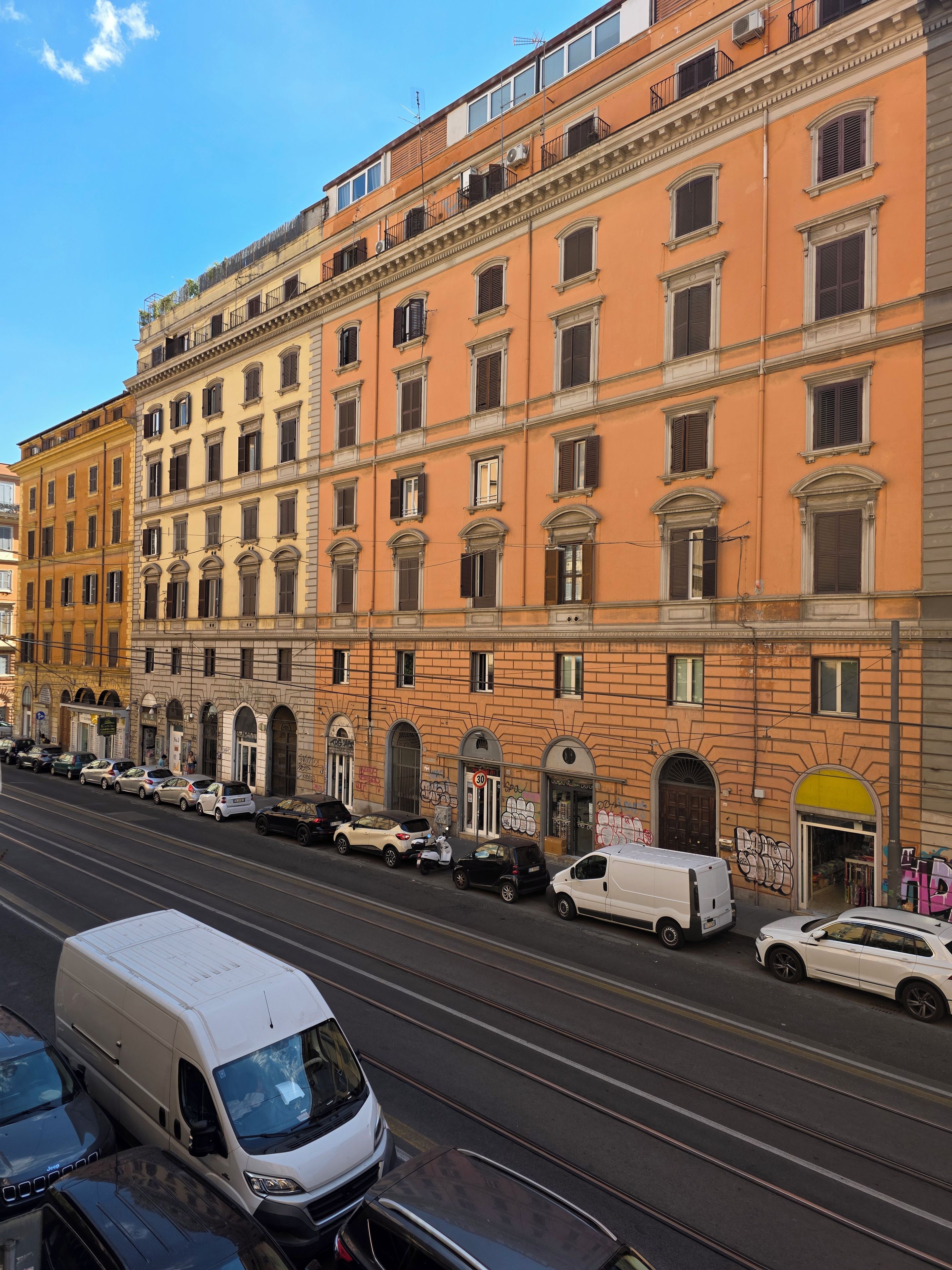A multi-story building with a row of parked cars and a tram line in front.