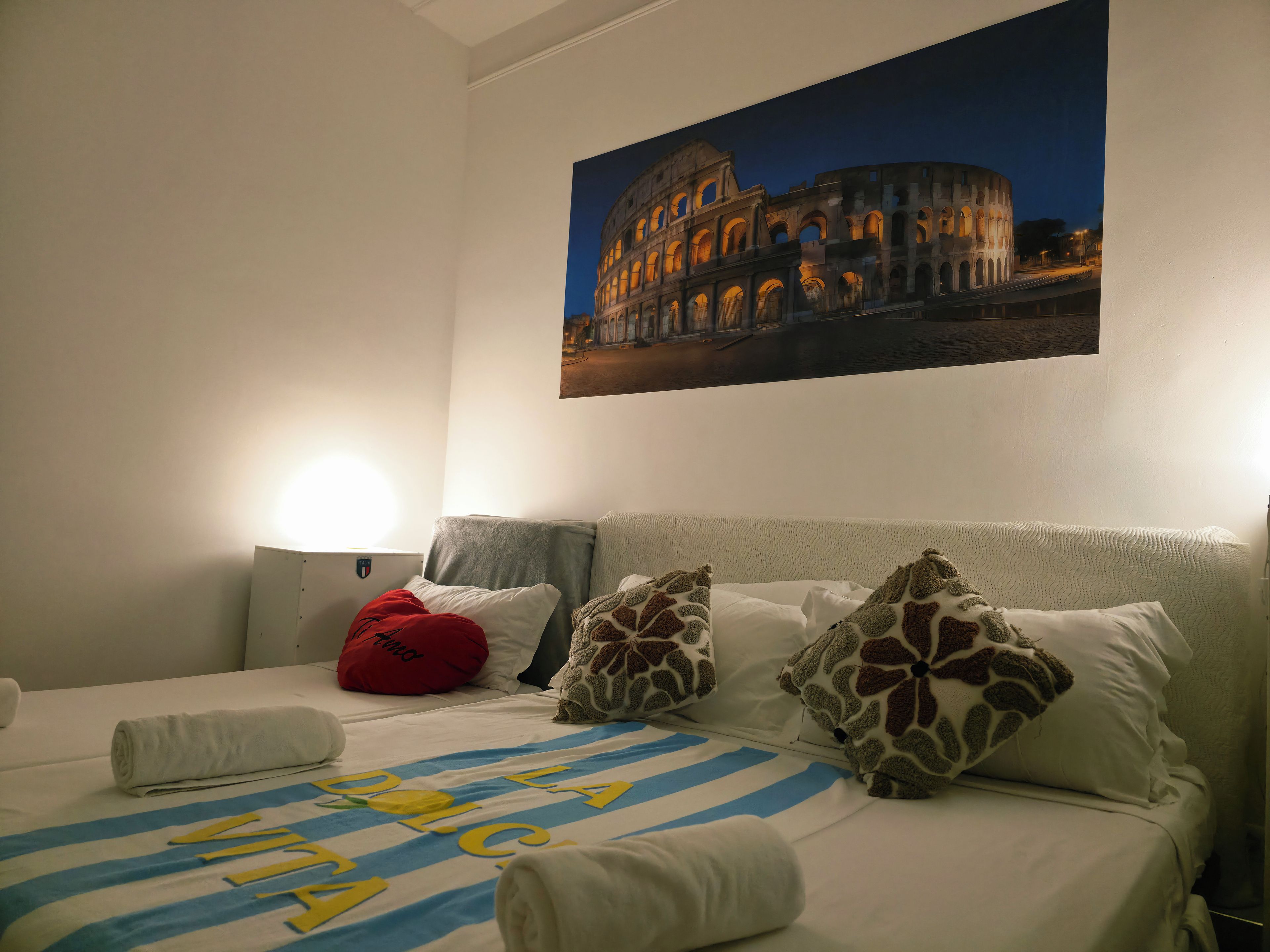 A hotel room with a bed featuring a striped bedspread, a pillow with a giraffe pattern, and a red pillow.