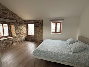 Ein Schlafzimmer mit schrägen Wänden, einem Bett mit gemusterten Betttextilien und zwei Fenstern.