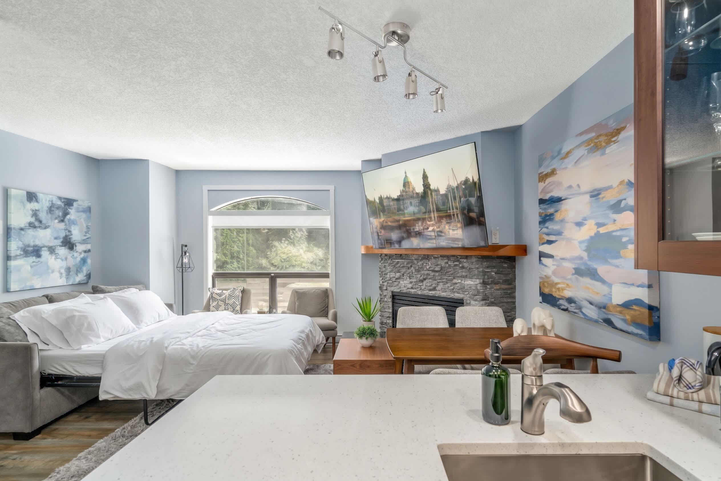 Une chambre moderne avec un lit, un bureau et une vue sur le paysage urbain, visible par la fenêtre.