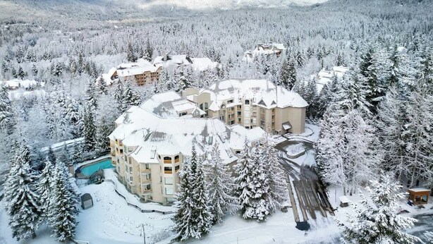 Ein schneebedecktes Resort mit mehreren Gebäuden, einem Schwimmbad und einer Bergkulisse.
