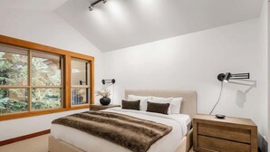 Ein Schlafzimmer mit großem Fenster, einem Bett mit Felldecke, einem Nachttisch und einer Wandleuchte.