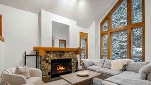 Ein Wohnzimmer mit Kamin aus Stein, großen Fenstern, einer Couch und einem Couchtisch.