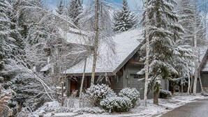 Eine schneebedeckte Holzhütte, umgeben von dichten Nadelbäumen.