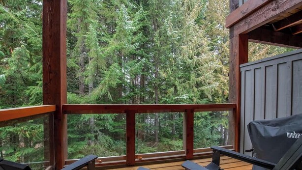 Eine Holzterrasse mit Blick auf dichten Wald, einem Grill und zwei Liegestühlen.