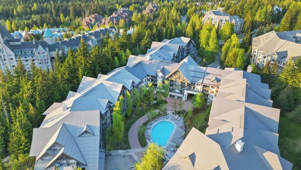 A resort with multiple buildings, a central pool, and surrounding forest. - Luxe 2-Bed Ski-in Ski-out, On Hill (Whistler)