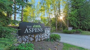 A sign for 'The Aspens' with a stone wall and greenery. - Luxe 2-Bed Ski-in Ski-out, On Hill (Whistler)