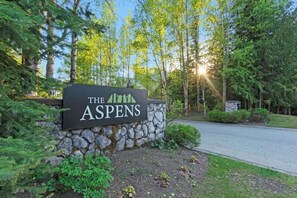 A sign for 'The Aspens' with a stone wall and greenery. - Luxe 2-Bed | Ski-in Ski-out | On Hill (Whistler)