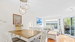 A modern dining area with a wooden table and white chairs, a sofa, and a large window with a view. - Luxe 2-Bed Ski-in Ski-out, On Hill (Whistler)