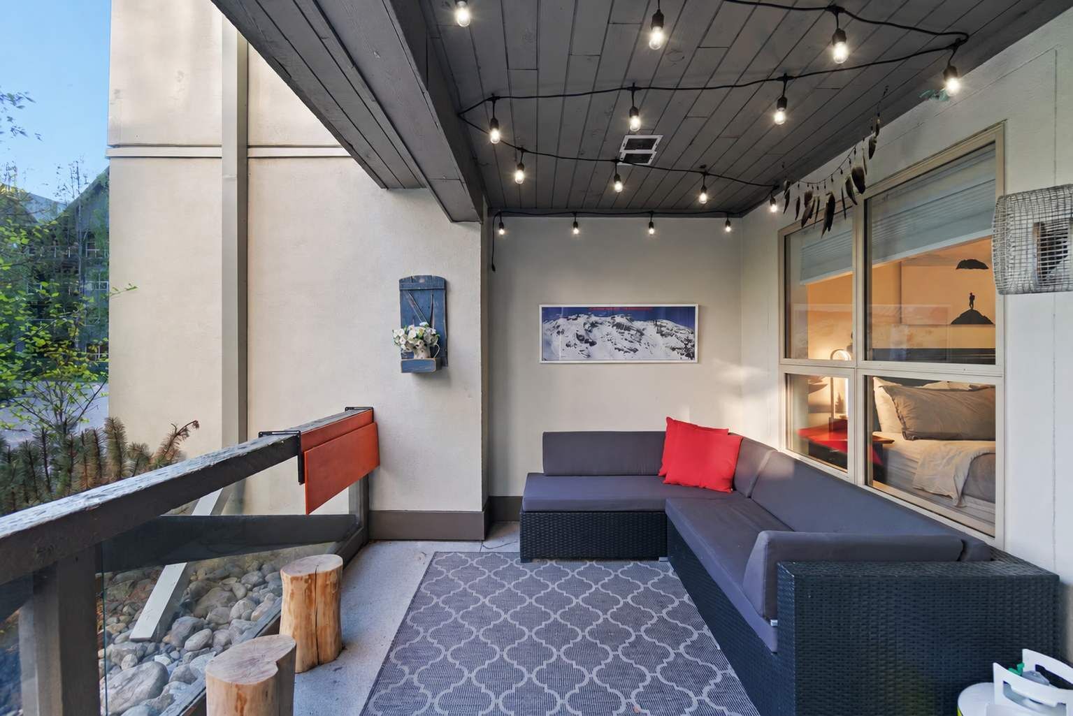 An outdoor seating area with a sofa and a dining table, a wooden bench, and a patterned rug.