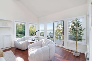 A modern living room with a curved sofa, a telescope, and a potted tree. - Ocean View Luxury Retreat in West Vancouver (West Vancouver)