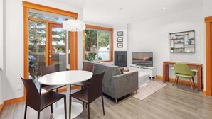 A modern living room with a dining area, a grey sofa, a TV, and a small table with a chair. - Symphony - Walk to village & slopes - Luxury 4-bed (Whistler)