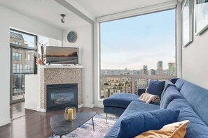 Ein modernes Wohnzimmer mit Kamin, einer großen Couch, einem Flachbildfernseher und Blick auf die Stadt.