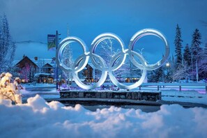 Un espace extérieur enneigé, avec les anneaux olympiques illuminés en arrière-plan.
