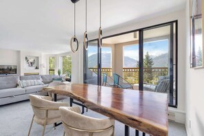 Ein modernes Wohnzimmer mit einem Holzesstisch, zwei Stühlen, einer Couch und einem Balkon mit Bergblick.