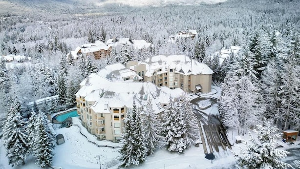 Un complejo turístico nevado con varios edificios, una piscina y montañas al fondo.