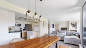 Una cocina moderna con armarios blancos, una mesa de comedor de madera y lámparas colgantes.