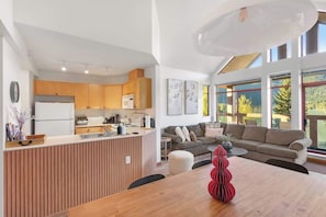 A modern kitchen with wooden cabinets, a central island, and a dining area with a wooden table and red decorative item.