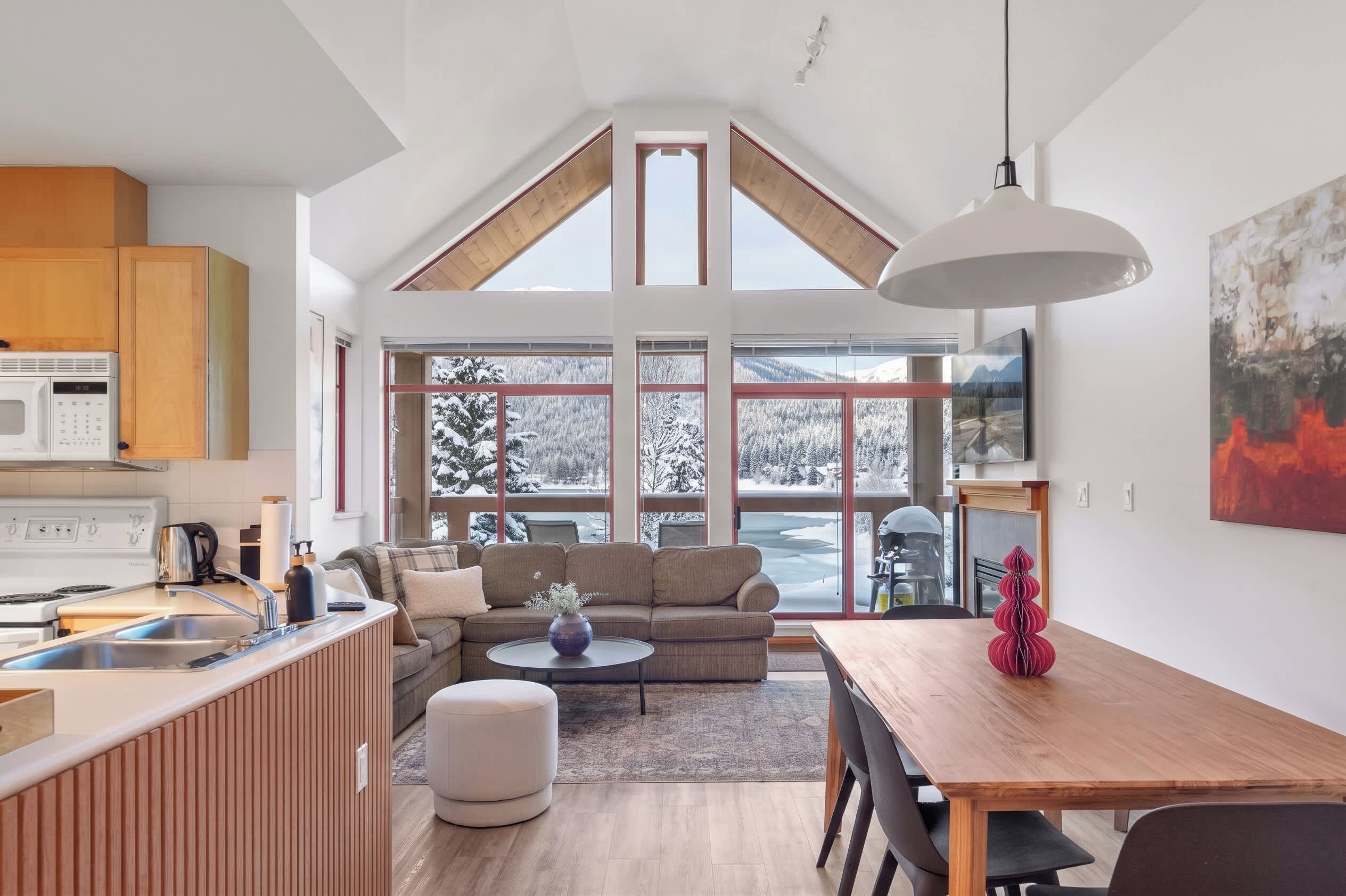 A modern kitchen with a dining area, large windows, and a loft space.