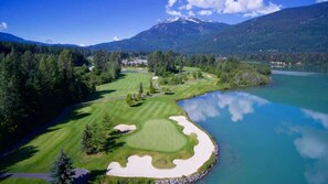 Ein Golfplatz mit See, umgeben von Wald und Bergen.