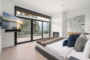 A modern bedroom with a large bed, a flat-screen TV, and a sliding glass door leading to a balcony. - Timber Haven - Luxury Ski in Ski out - Kadenwood (Whistler)