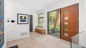 Um interior moderno com um banco de madeira, uma obra de arte emoldurada e uma porta de vidro deslizante para uma área externa.