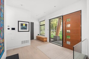A modern interior with a wooden bench, a framed artwork, and a sliding glass door leading to an outdoor area. - Timber Haven - Luxury Ski in Ski out - Kadenwood (Whistler)