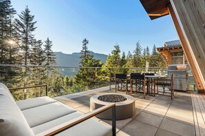 Ein Balkon mit einer Couch, einer Feuerstelle, einem Essbereich mit Stühlen und einem Tisch sowie einem Grill.