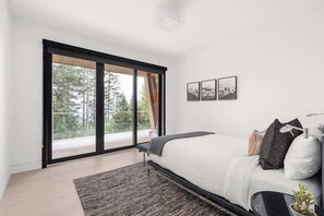 A modern bedroom with a large bed, a sliding glass door leading to a balcony, and framed pictures on the wall. - Timber Haven - Luxury Ski in Ski out - Kadenwood (Whistler)