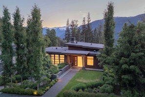 A modern house with a sloped roof, surrounded by dense trees and a mountain backdrop. - TimberVue  - Luxury Ski in Ski out - Kadenwood (Whistler)
