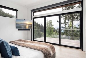 Ein modernes Schlafzimmer mit einem großen Bett, einem an der Wand montierten Fernseher und einem Balkon mit schöner Aussicht.
