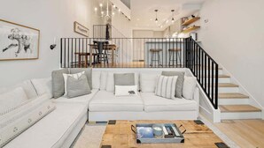 A modern living room with a sectional sofa, a coffee table, and a staircase with a black railing. - Luxe 5-BED Scandinave Retreat - Walk to Slopes (Whistler)