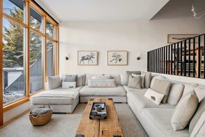 Una sala de estar moderna con un sofá modular, una mesa de centro de madera y grandes ventanales.