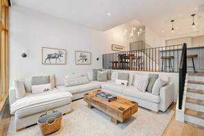 Una sala de estar moderna con un sofá modular, una mesa de centro de madera y una escalera con barandilla.