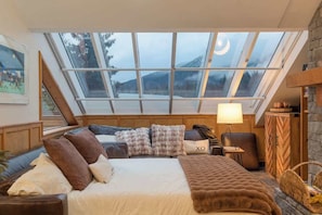 A bedroom with a skylight, a bed with a blanket, a bedside table with a lamp, and a wooden wardrobe. - Whistler Village | Penthouse | 4-Bed (Whistler)