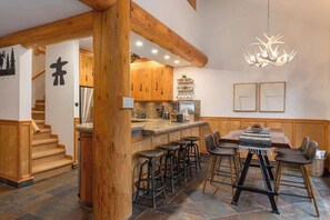 Cozinha com vigas de madeira, área de bar com banquetas, um lustre e uma escada.