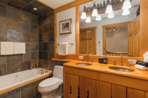 Ein Badezimmer mit einer Badewanne, zwei Waschbecken, einer Toilette und einem Spiegel.
