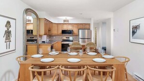 Un comedor con mesa y sillas de madera, una cocina con armarios y electrodomésticos de madera, y un cuadro enmarcado en la pared.