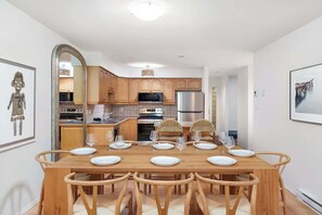 A dining area with a wooden table and chairs, a kitchen with wooden cabinets and appliances, and a framed picture on the wall.