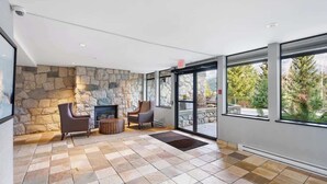Una habitación amplia con pared de piedra, una chimenea, dos sillones y ventanas grandes.