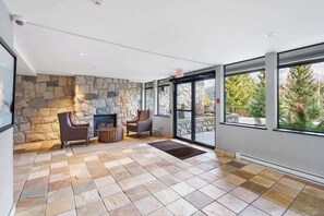A spacious room with a stone wall, a fireplace, two chairs, and large windows.