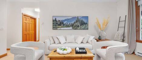 Ein Wohnzimmer mit einer Couch, zwei Sesseln, einem Couchtisch, einem Gemälde und einer Vase mit Trockenpflanzen.