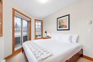 Une chambre avec un grand lit, une fenêtre donnant sur des arbres couverts de neige et un tableau encadré accroché au mur.