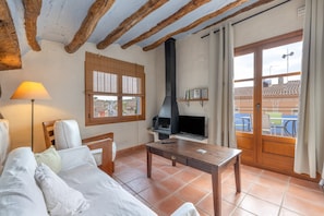 A living room with a sofa, a wooden table, a TV, a grill, and a window with blinds. - Apartment 'Cal Capdevila Dúplex' with Mountain View, Wi-Fi and Air Conditioning (Pira)