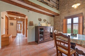 Un coin repas comprenant une table en verre, des chaises en bois, un meuble avec des tiroirs et un mur en pierre.