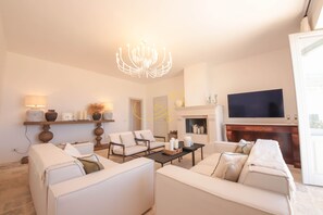 Ein geräumiges Wohnzimmer mit Kamin, einer Kristallleuchter und einem Flachbildfernseher.