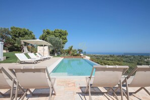 Ein Poolbereich mit Liegestühlen und Blick auf das Meer.